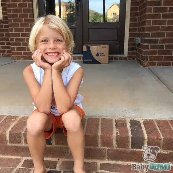 little boy sitting on porch and Blue Apron box in background