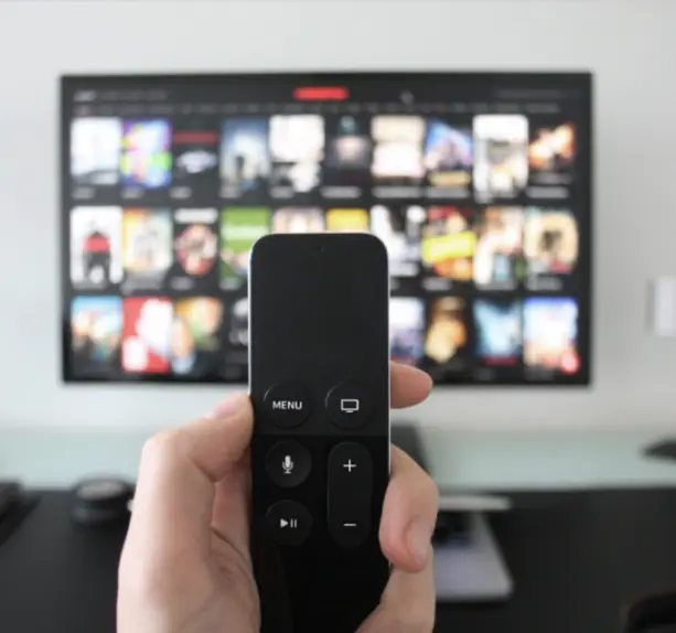 tv remote in hand blurred background with netflix on tv
