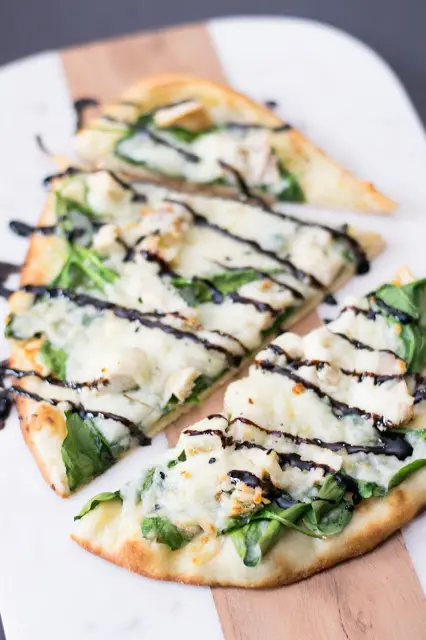 chicken and spinach pizza cut into pieces on cutting board