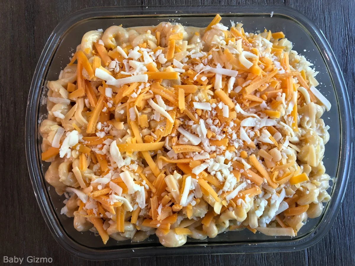 Homemade mac and cheese in glass dish with shredded cheese on top.