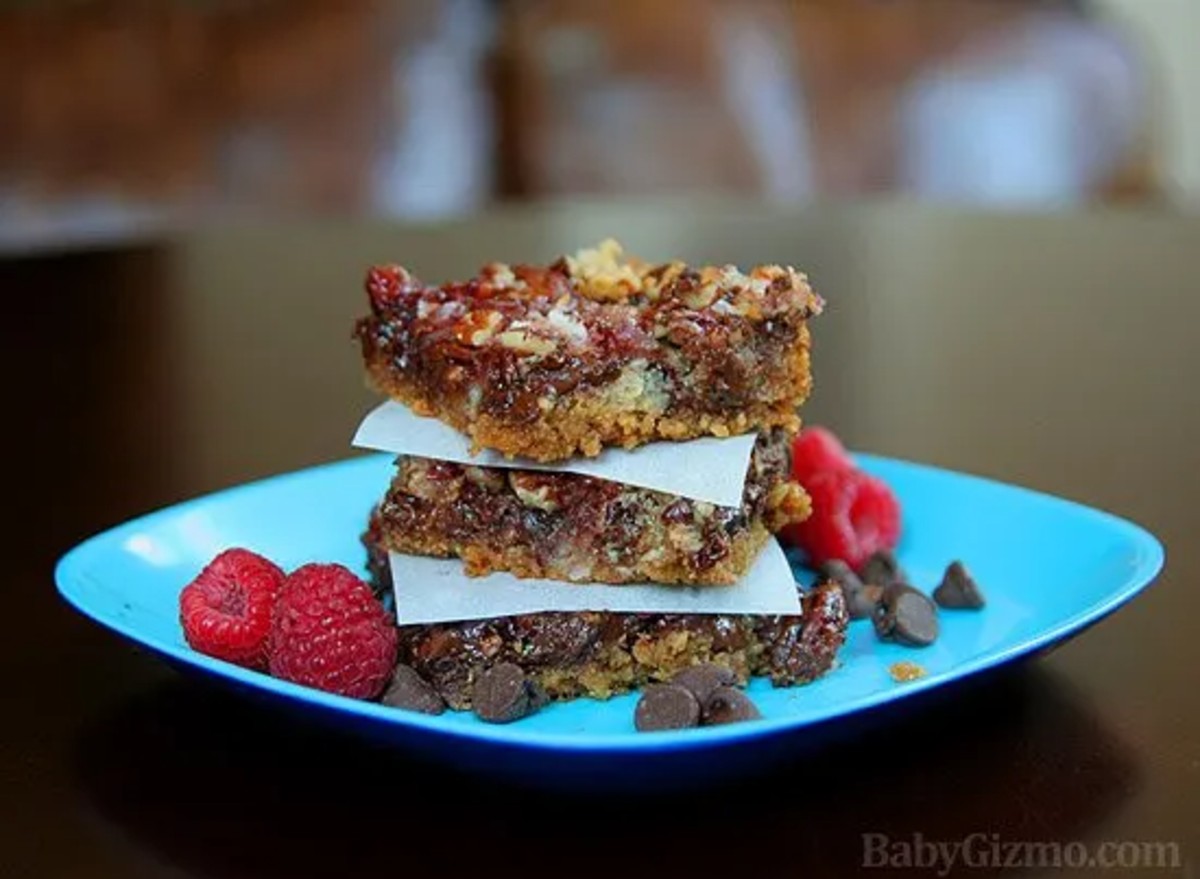 3 raspberry magic bars stacked on top of each other on a blue plate with raspberries and chocolate chips on the side  