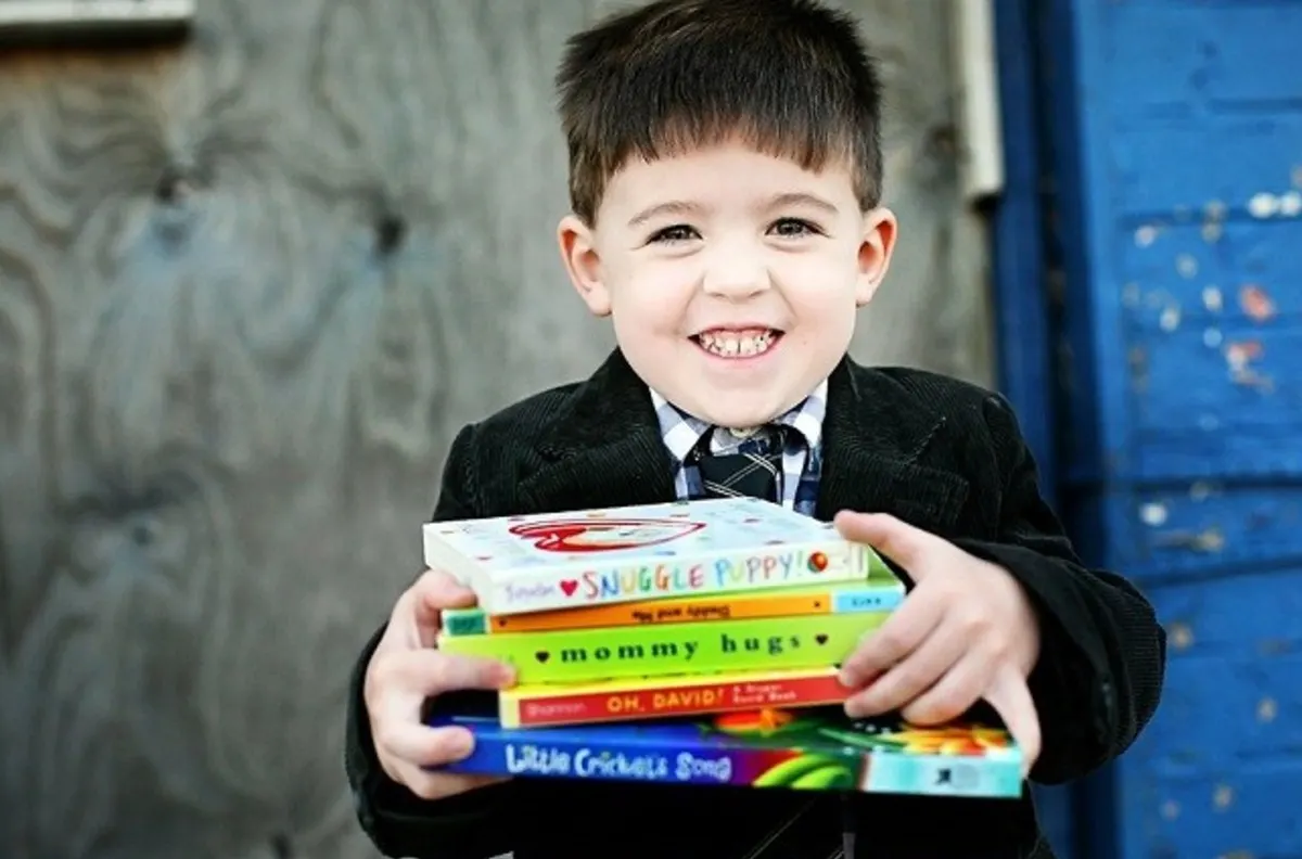 little boy holding stacks of books