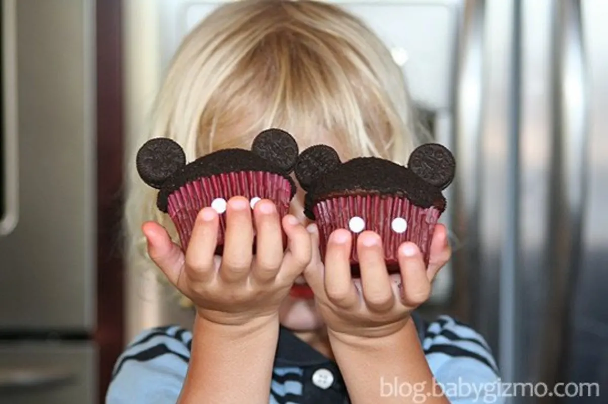 a kid holding two mickey mouse cupcakes in each hand 