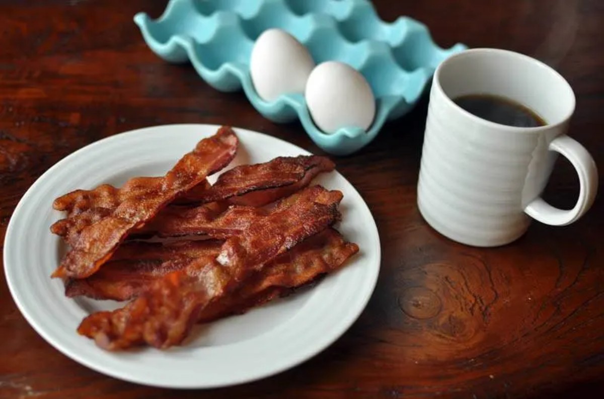 bacon on a white plate with coffee and egg next to it 